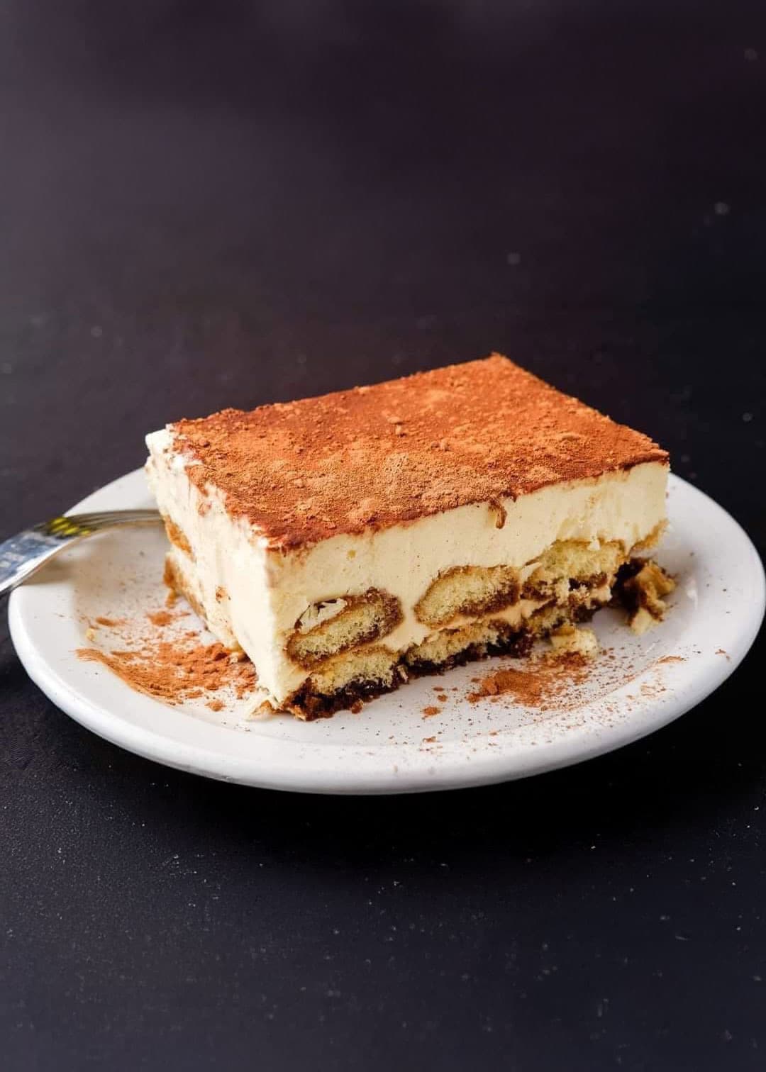A slice of tiramisu dusted with cocoa on a white plate