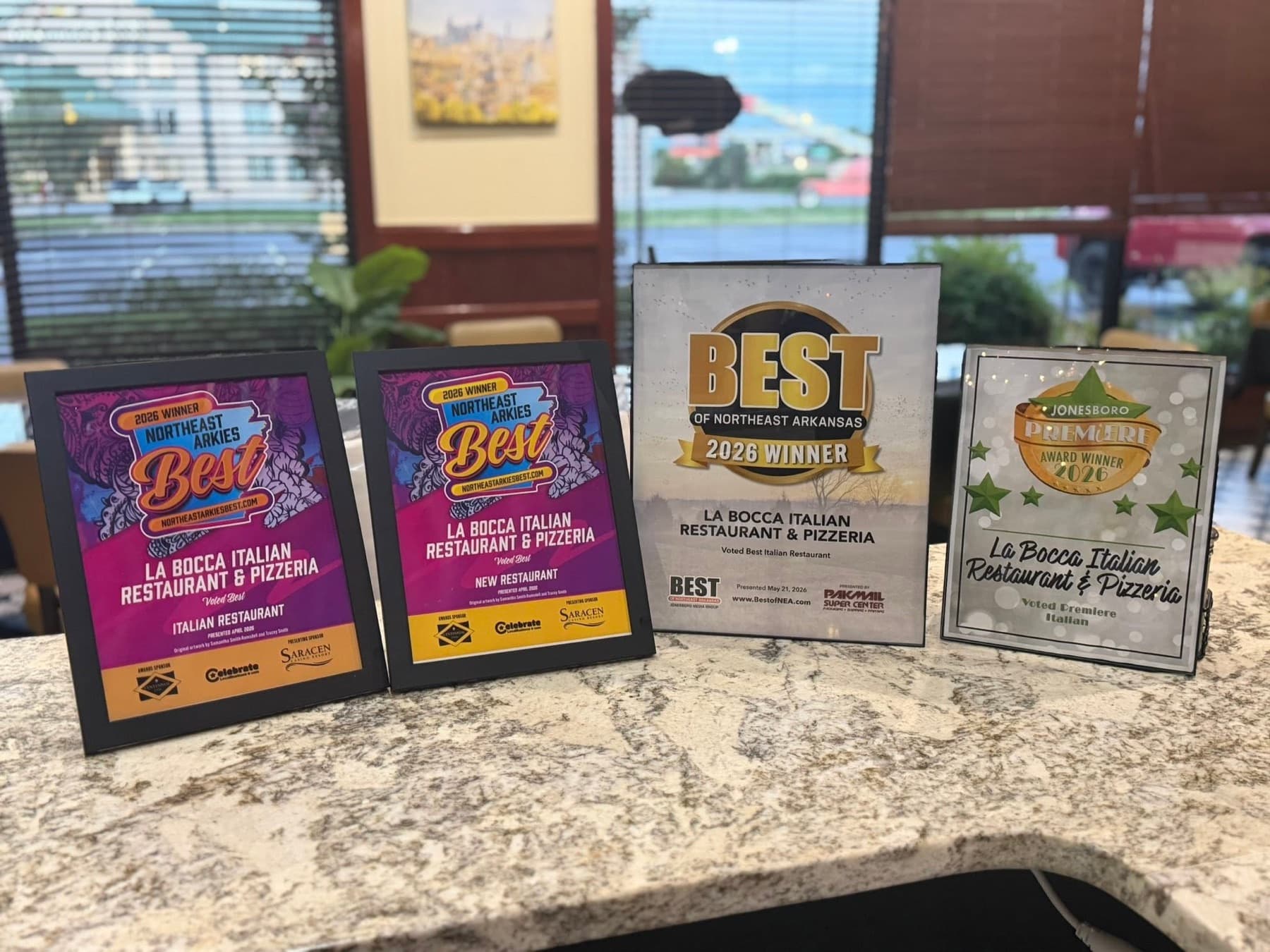 La Bocca's four 2026 award plaques lined up on the granite counter: Northeast Arkies Best Italian and Best New Restaurant, Best of Northeast Arkansas, and Jonesboro Premiere Italian