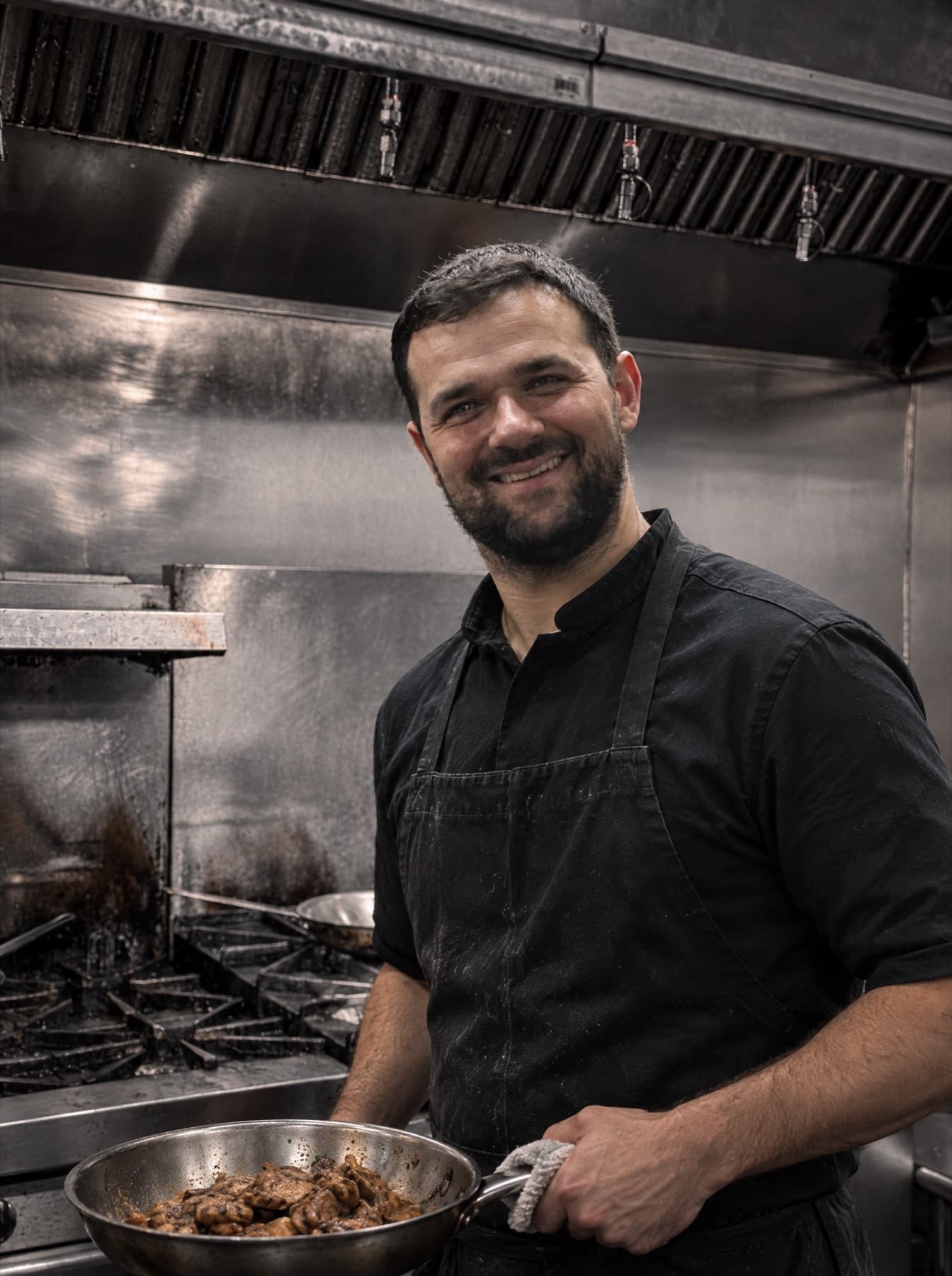 Rinor Neziri smiling at the stove in the La Bocca kitchen, pan in hand